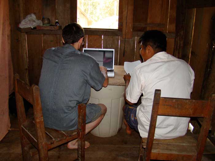 Javier Ruedas and Alfredo Barbosa sit by a laptop. Alfredo Barbosa holds a sheaf of papers while Javier Ruedas types.